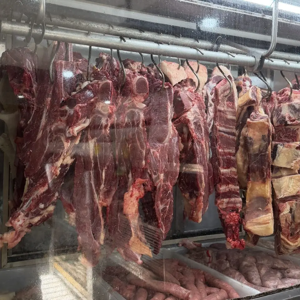 Balcão refrigerado do açougue, com cortes de carne bovina pendurados e linguiças expostas embaixo